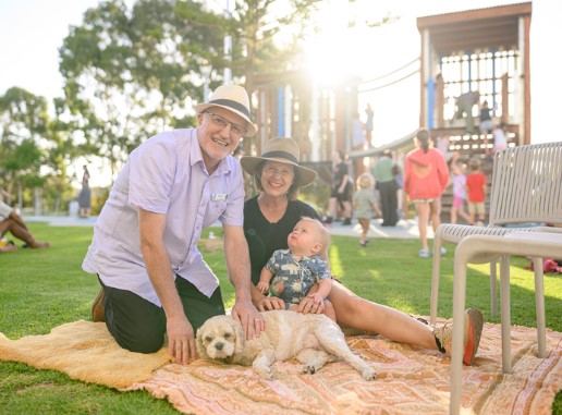 Mum, dad, baby and their dog sitting on a picnic rug at the East Fremantle community park